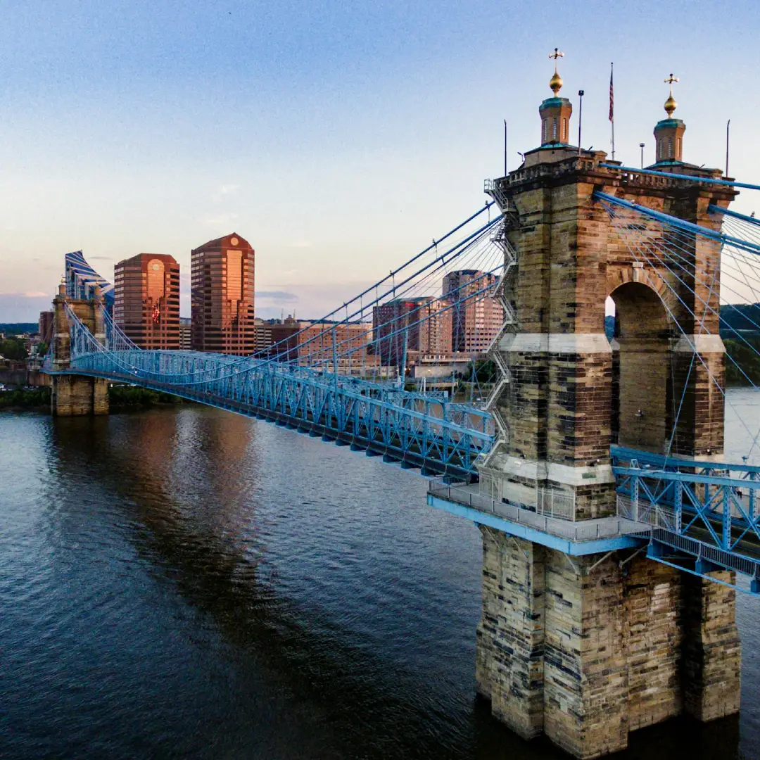 Suspension bridge over the river in Cincinnati with city buildings at sunset