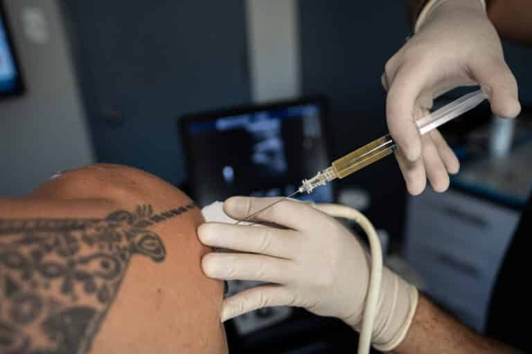 Ultrasound-guided shoulder injection: one gloved hand holds the probe while the other advances the needle
